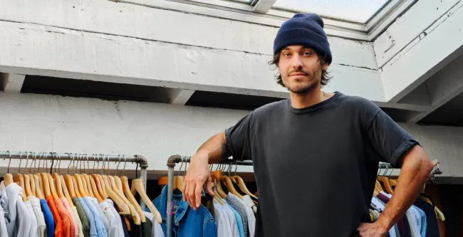 Man standing against a rack of clothes 
